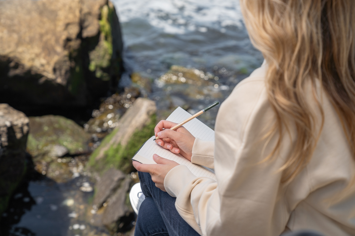 Woman Sitting By the Water and Writing in a Journal 